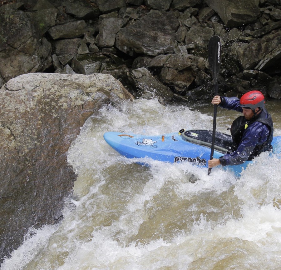 Jesse Pulliam paddling a blue kayak past a boulder